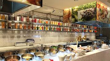 Uma área de buffet com diversas estações de comida, variedade de acompanhamentos e grande seleção de bebidas.