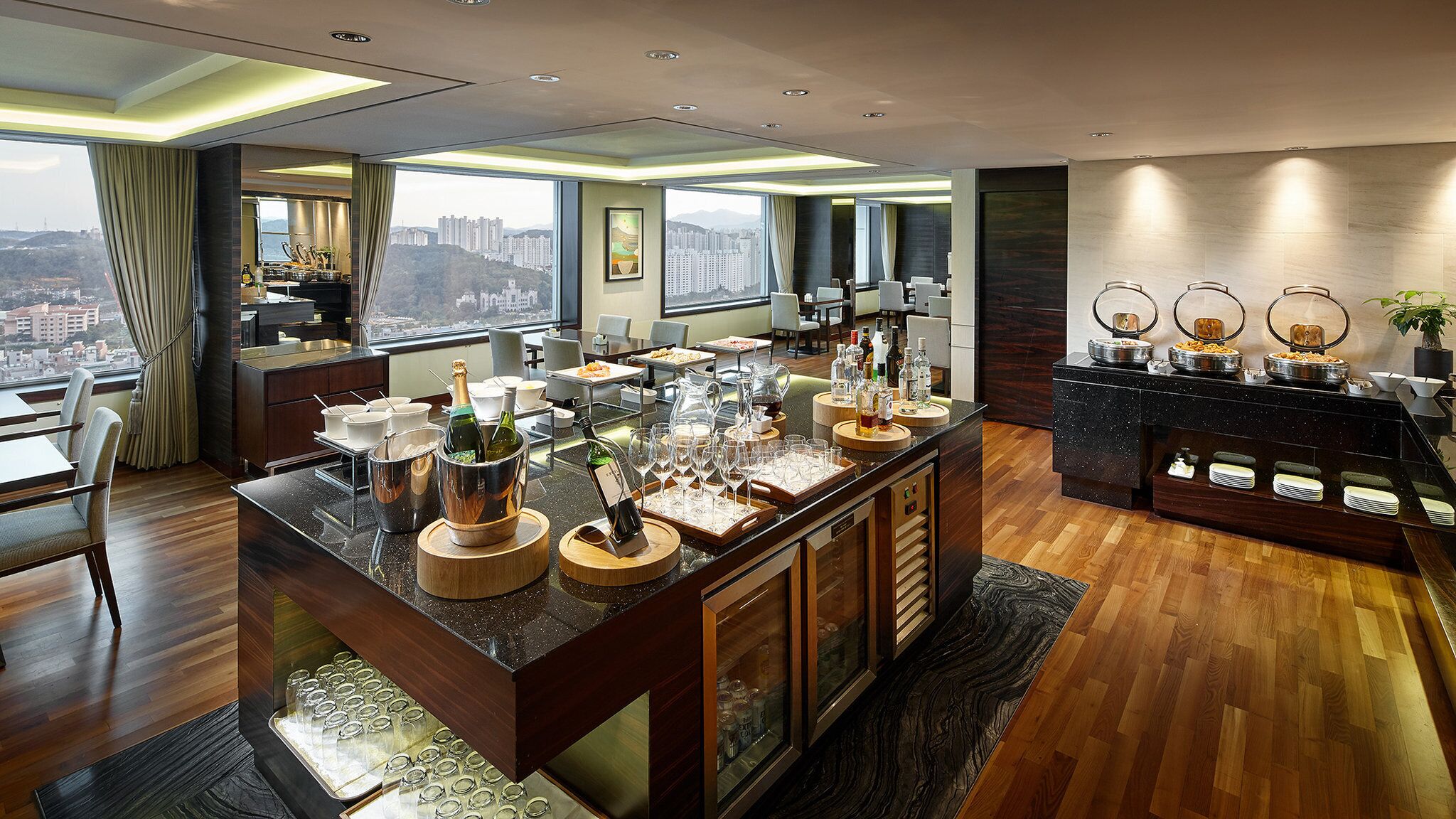 A modern hotel kitchen with a bar area, large windows, and a city view.