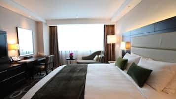 Habitación de hotel con una cama grande, un escritorio con computadora, un televisor y una ventana con cortinas.