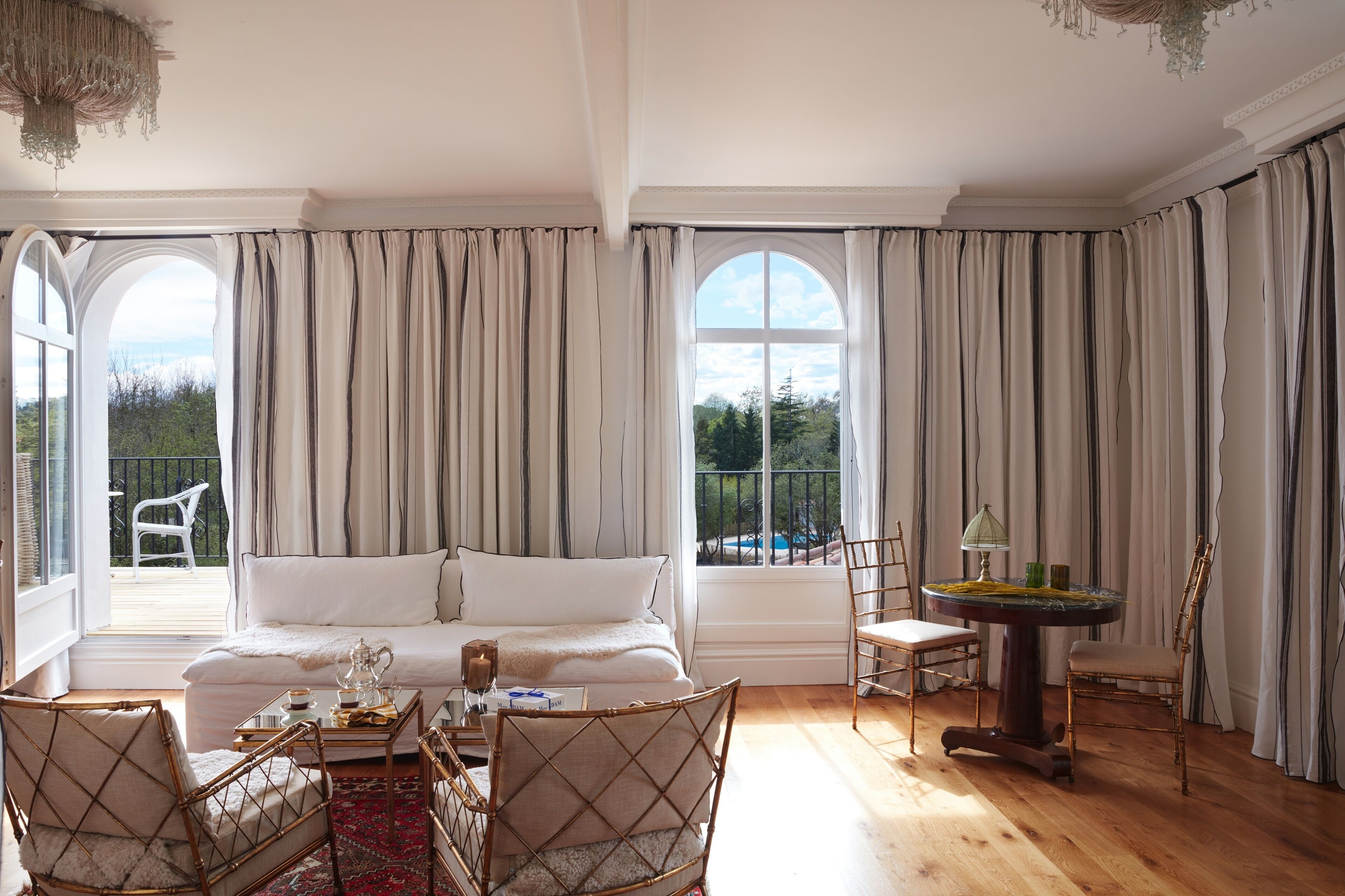 Una habitación amplia con un gran ventanal, un sofá, una mesa de comedor con sillas y una mesita de noche con lámpara.