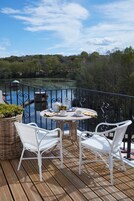 A deck with a table and chairs overlooking a lake, surrounded by a metal railing.