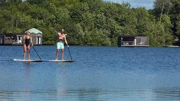 Kaksi ihmistä meloo suppilaudalla järvellä, taustalla näkyy taloja ja tiheää metsää.