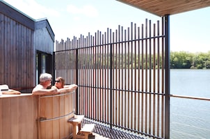 Una cabaña de madera con sauna, una terraza de madera y vistas a un lago.