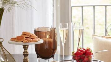 A table with a candle, two glasses of champagne, a plate of pastries, a vase with greenery, and a bowl of strawberries.