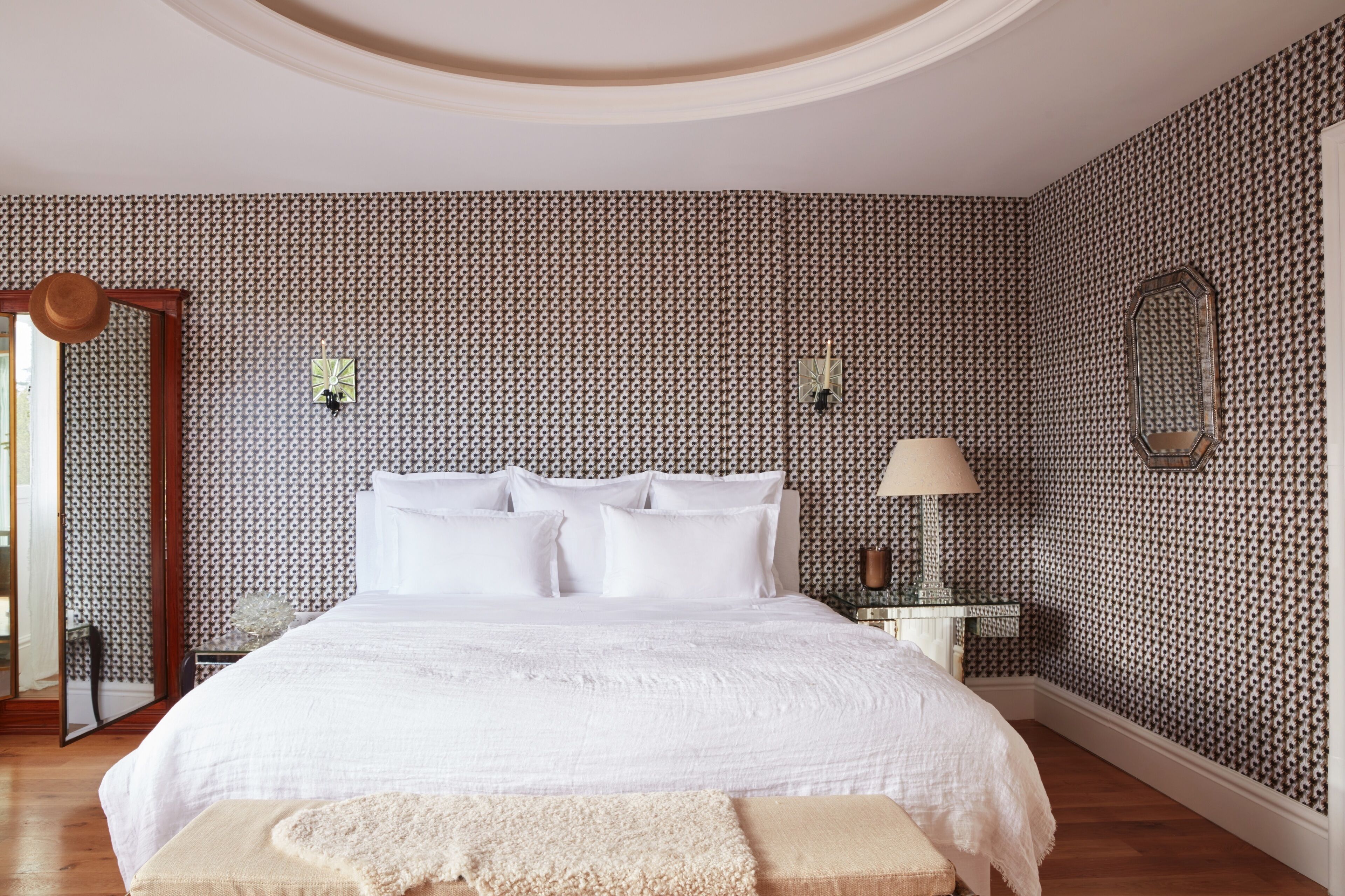Une chambre à coucher avec un grand lit, une table de chevet avec une lampe, un miroir et un papier peint à motifs.