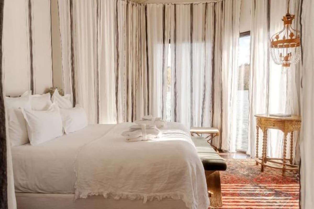 A hotel room with a large bed, a small table, and a decorative lamp.