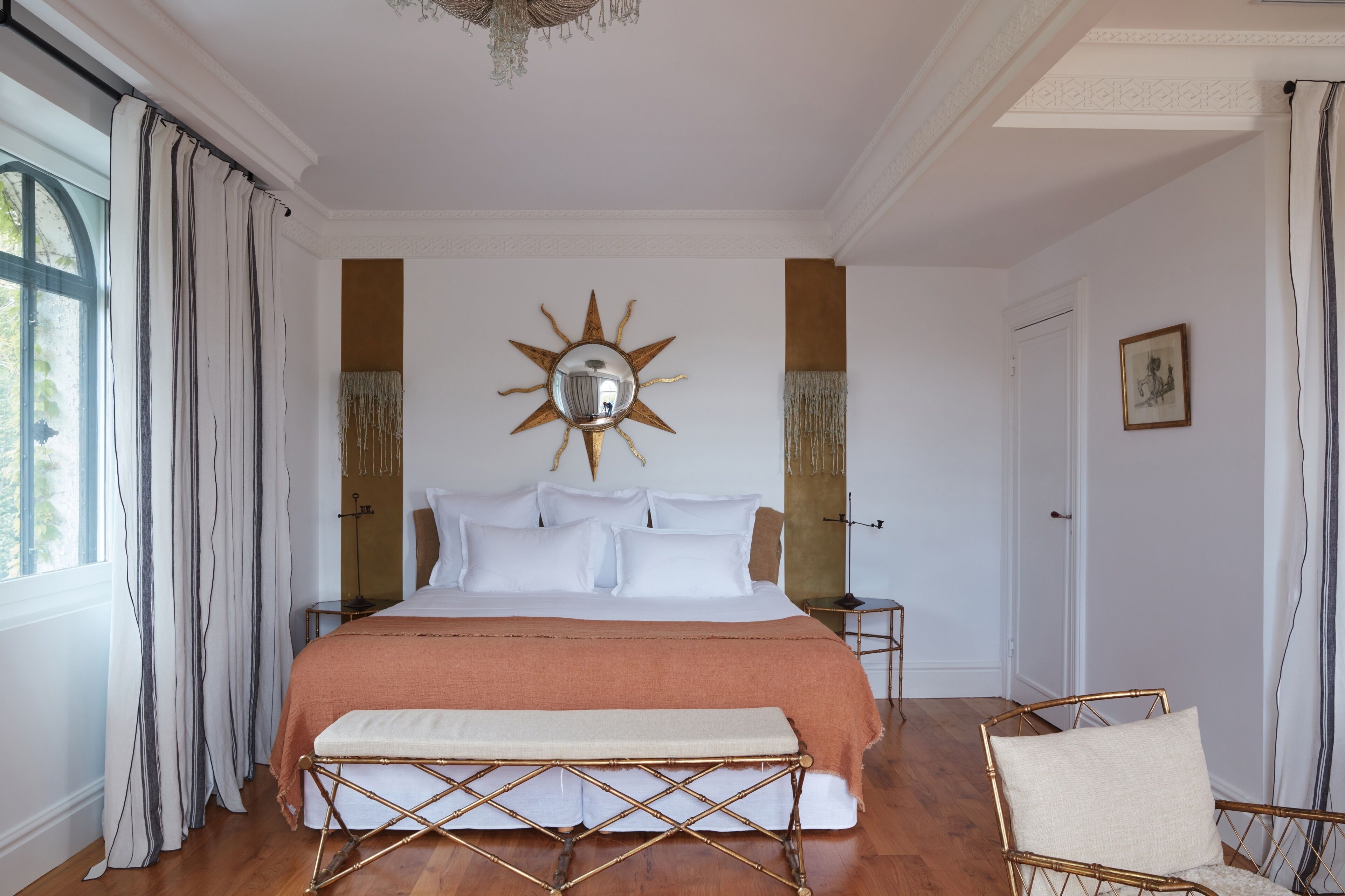 A bedroom with a large bed, a bench, a chair, a mirror, and a door.