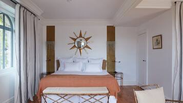 A bedroom with a large bed, a bench, a chair, a mirror, and a door.