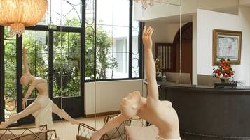 A room with a large mirror reflecting a sculpture of a dancer, a chandelier, and wicker furniture.