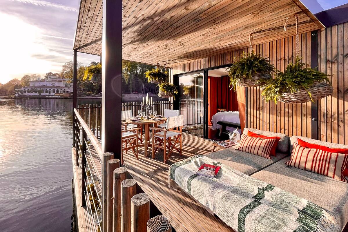 A wooden deck with a sofa and chairs, overlooking a body of water.