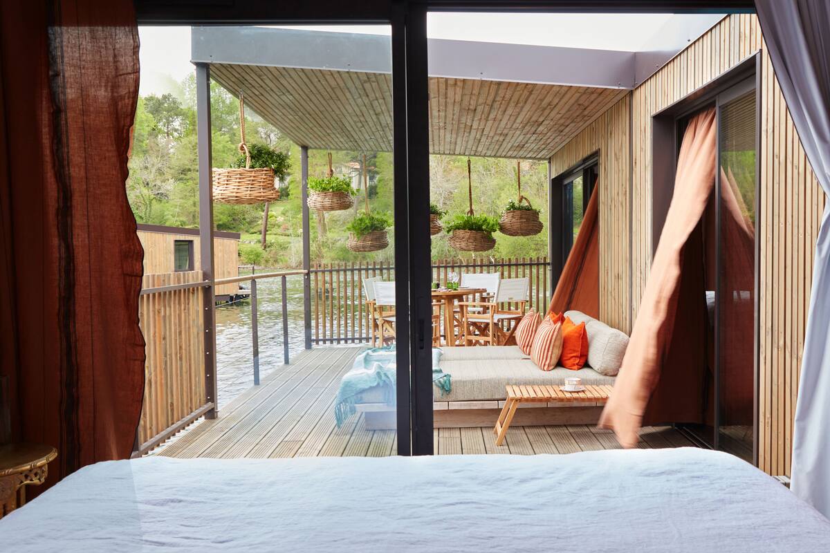 A bedroom with a large bed, a wooden deck, a sofa, and a table.