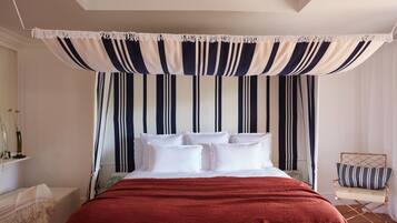 A bedroom with a bed, white pillows, a red blanket, a striped canopy, and a chair with a striped pillow.