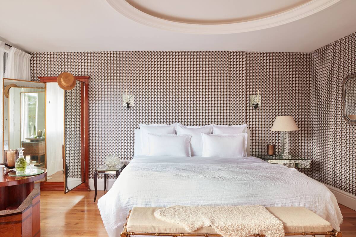 A bedroom with a large bed, a bedside table with a lamp, a mirror, and a dresser.