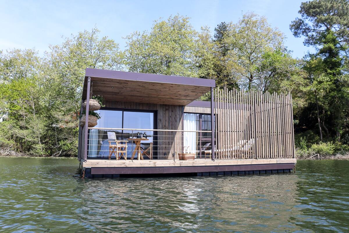 A floating house with a deck, windows, and a railing.