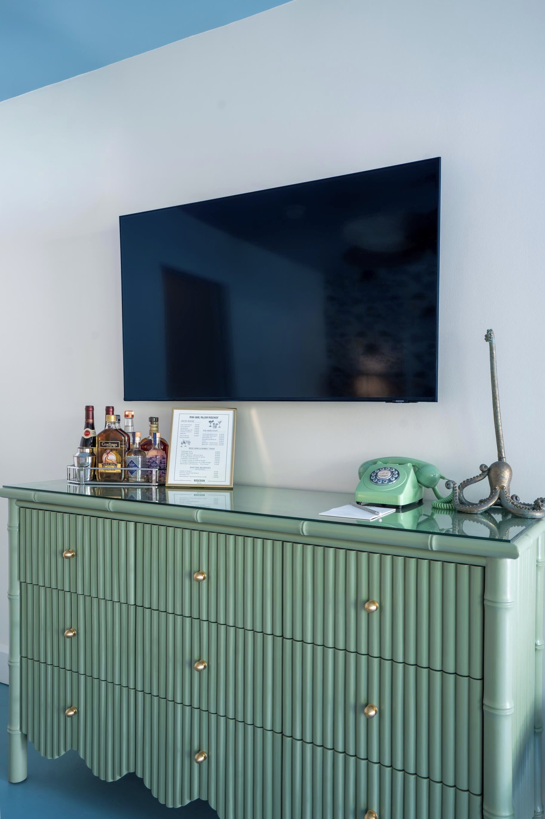 A room with a green cabinet, a mounted television, and a green telephone.