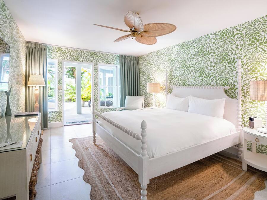 A bedroom with a bed, curtains, a ceiling fan, a bedside table, and a TV.