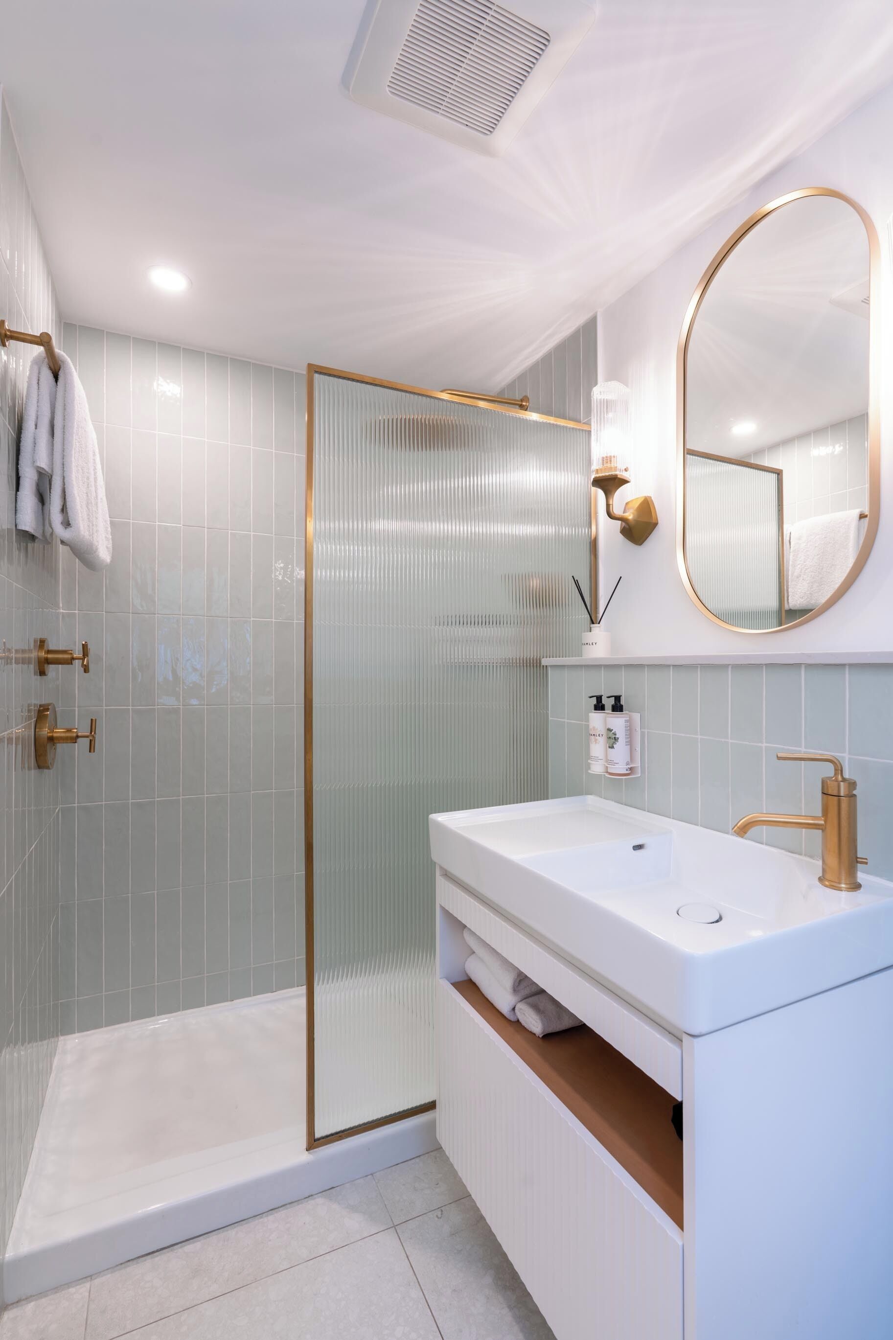 A modern bathroom with a glass shower enclosure, a white sink with gold fixtures, and a large mirror.