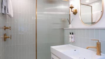 A modern bathroom with a glass shower enclosure, a white sink with gold fixtures, and a large mirror.