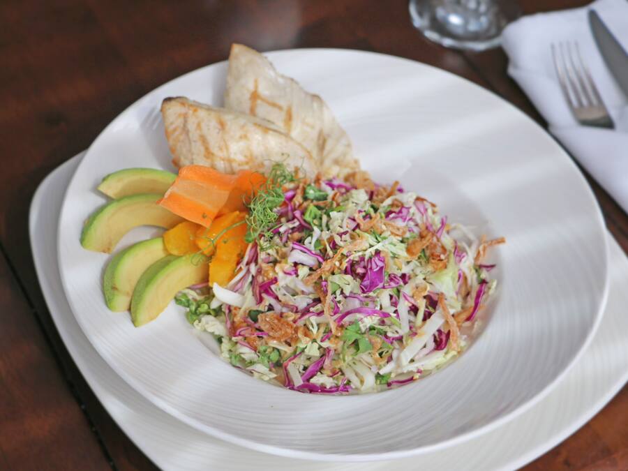 A plate with a salad, avocado slices, and grilled chicken on a white plate.