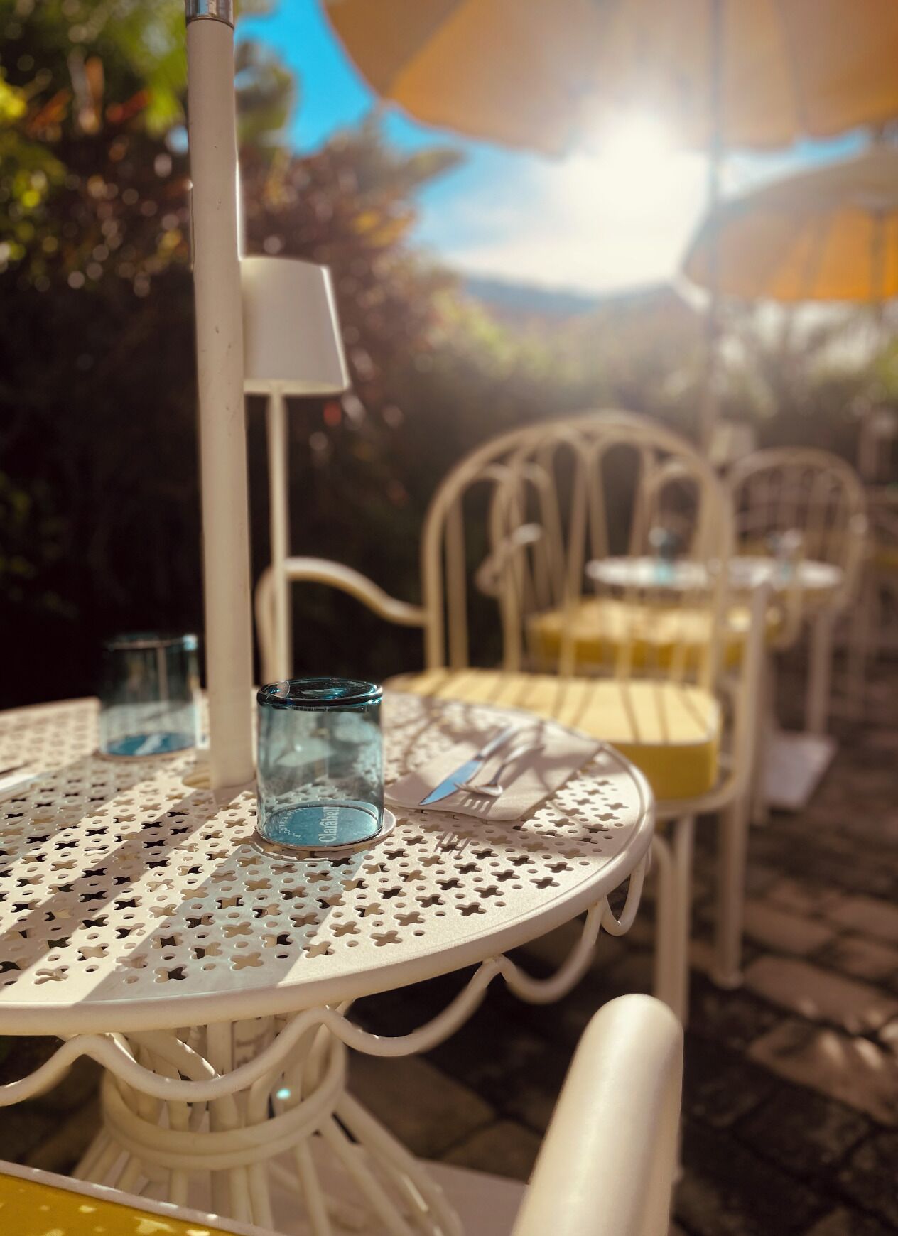 A round outdoor table with a white metal frame and a blue glass.