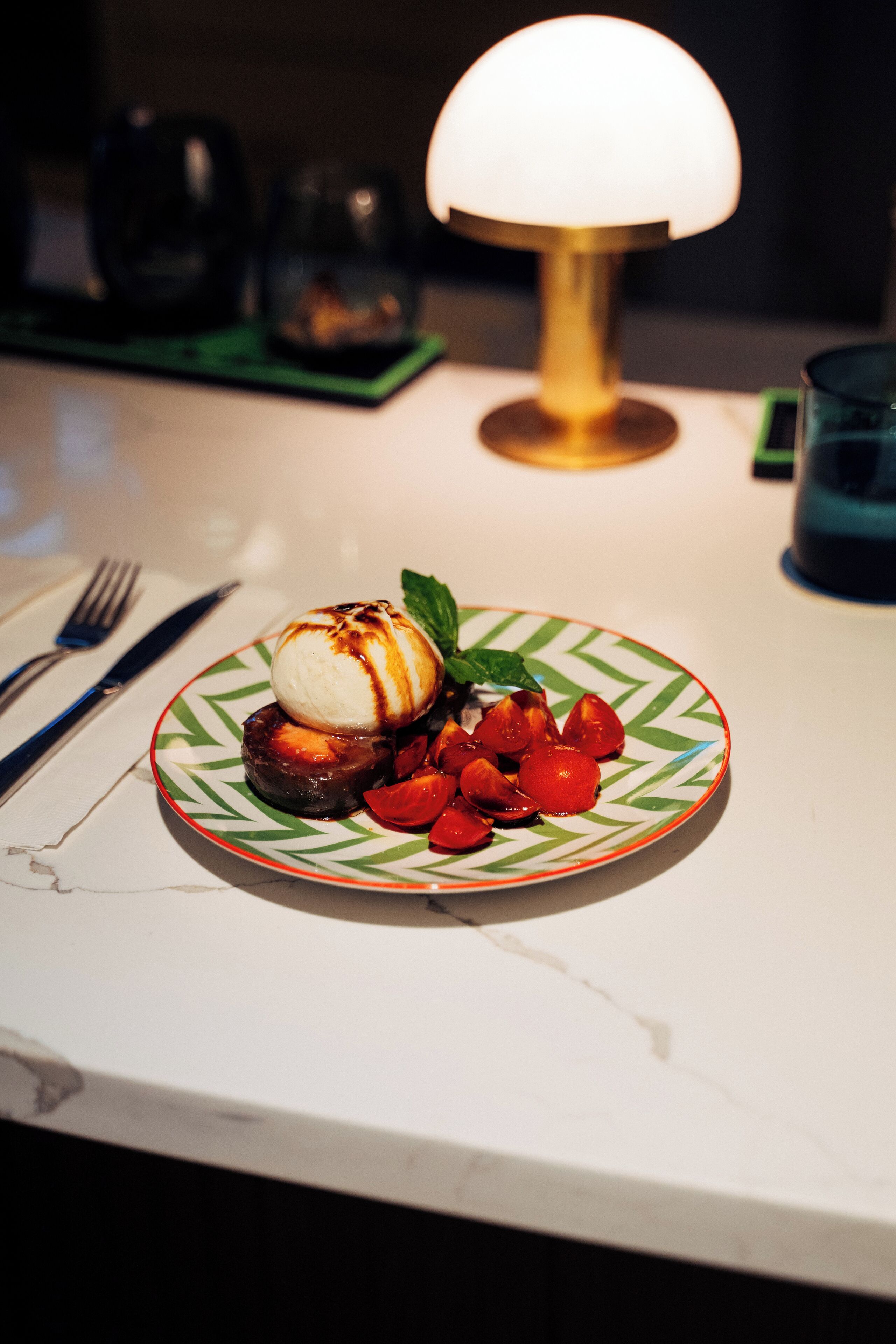 A dessert plate with a scoop of ice cream, a chocolate piece, and cherry tomatoes on a patterned plate.