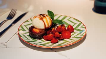 A dessert plate with a scoop of ice cream, a chocolate piece, and cherry tomatoes on a patterned plate.