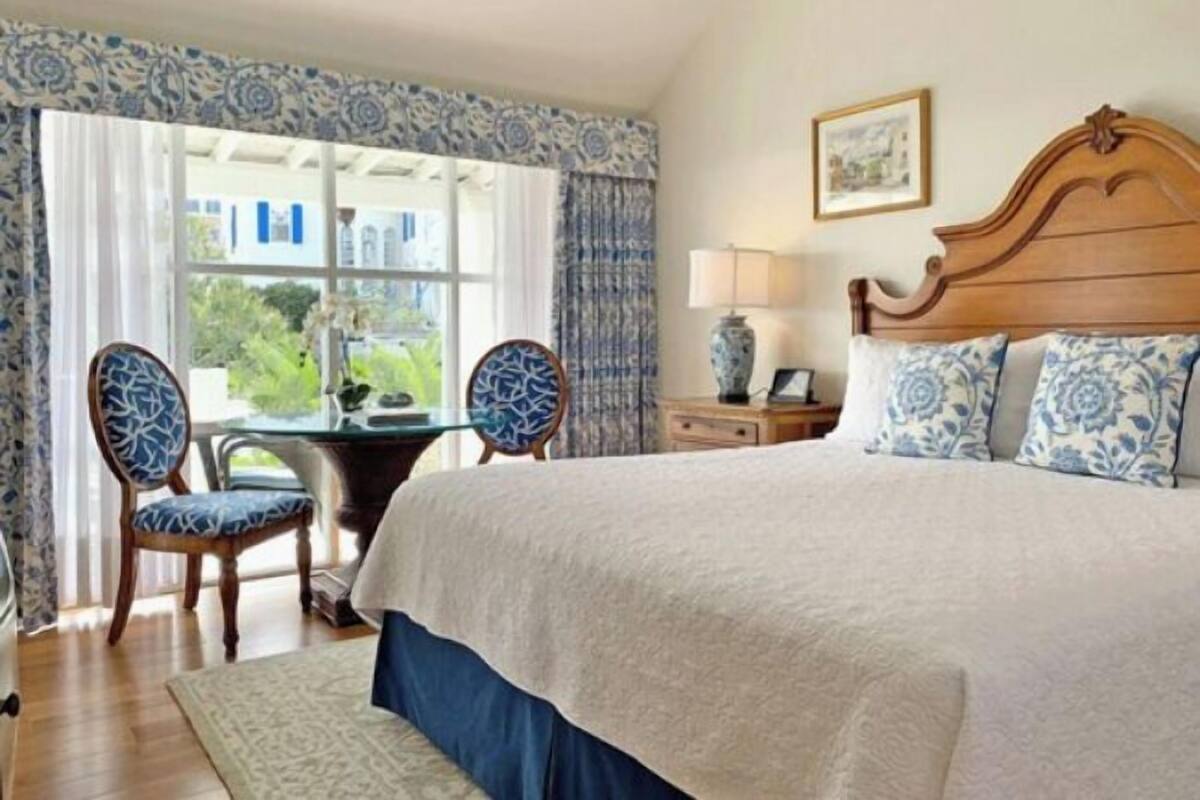 A bedroom with a large bed, two chairs, a small table, and a window with curtains.