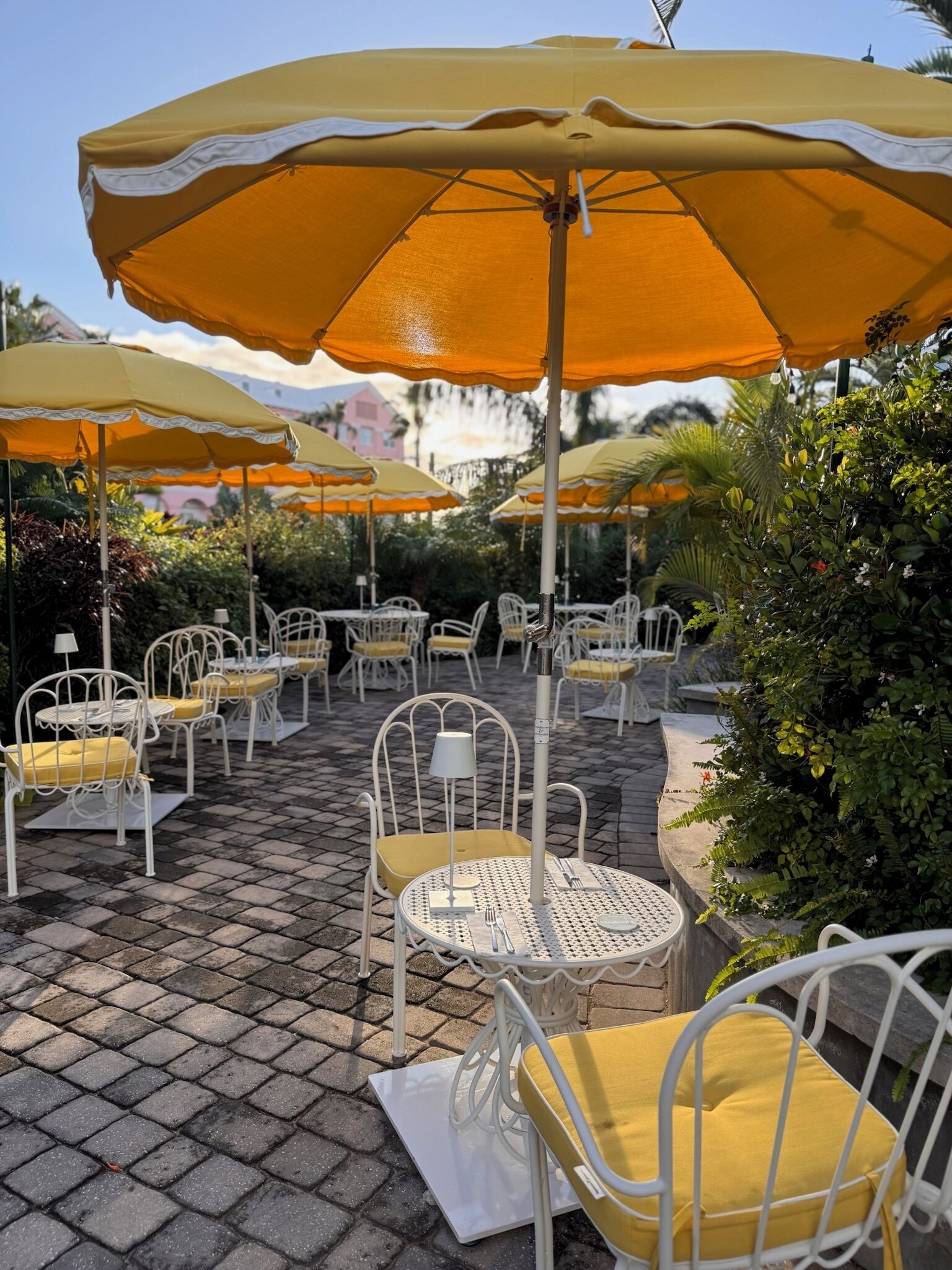 Udendørs siddepladser med gule og hvide parasoller, hvide metalstole og en belagt terrasse.