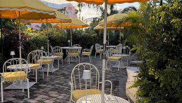 Udendørs siddepladser med gule og hvide parasoller, hvide metalstole og en belagt terrasse.