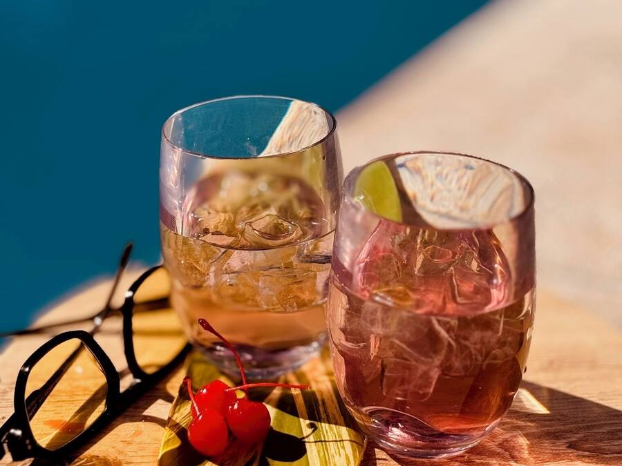Twee glazen drank op een houten dienblad met een paar brillen en kersen.