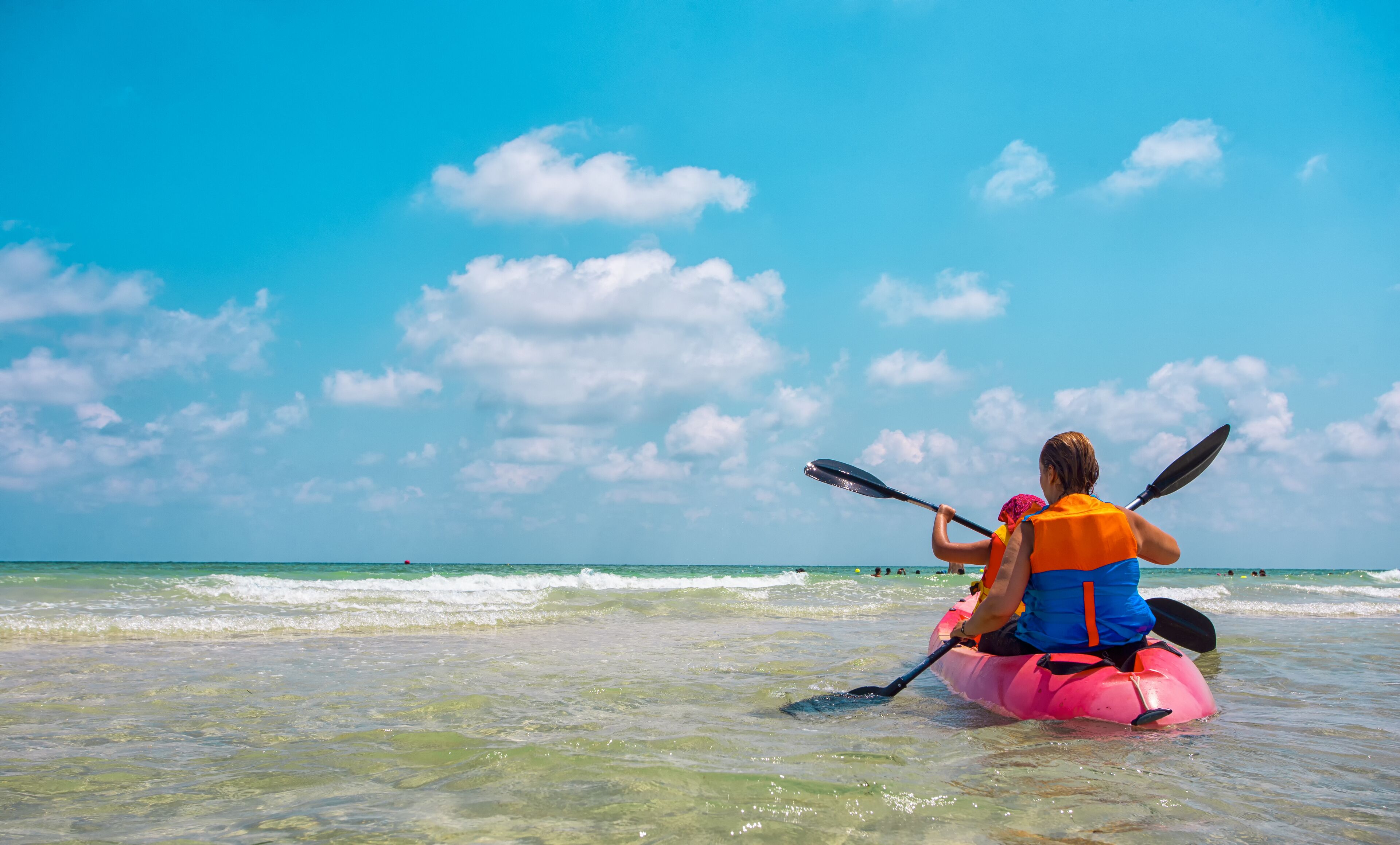 A person kayaking on a beach with clear skies and calm waters.