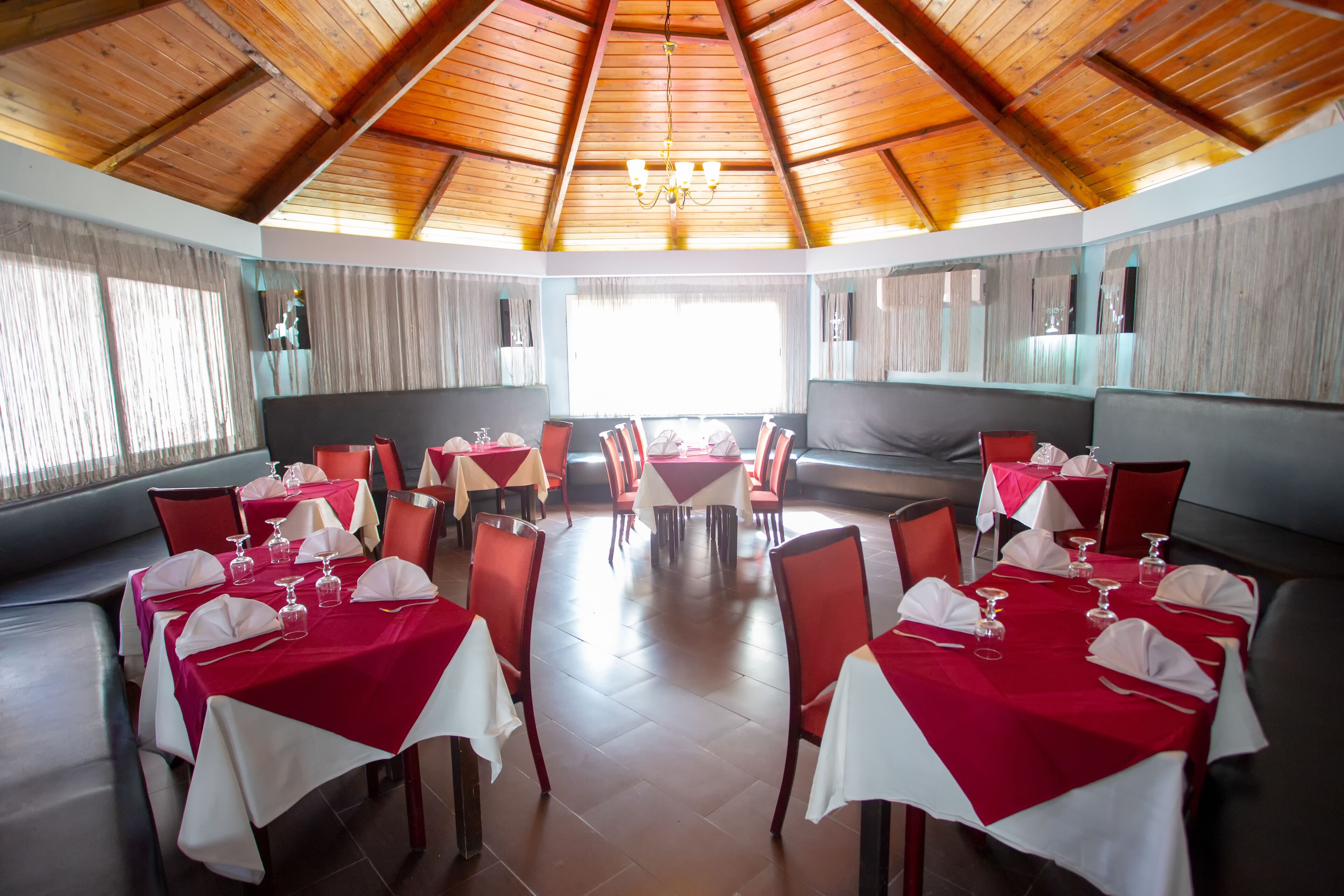 A restaurant with multiple tables set for dining, featuring red and white tablecloths and wooden ceiling beams.