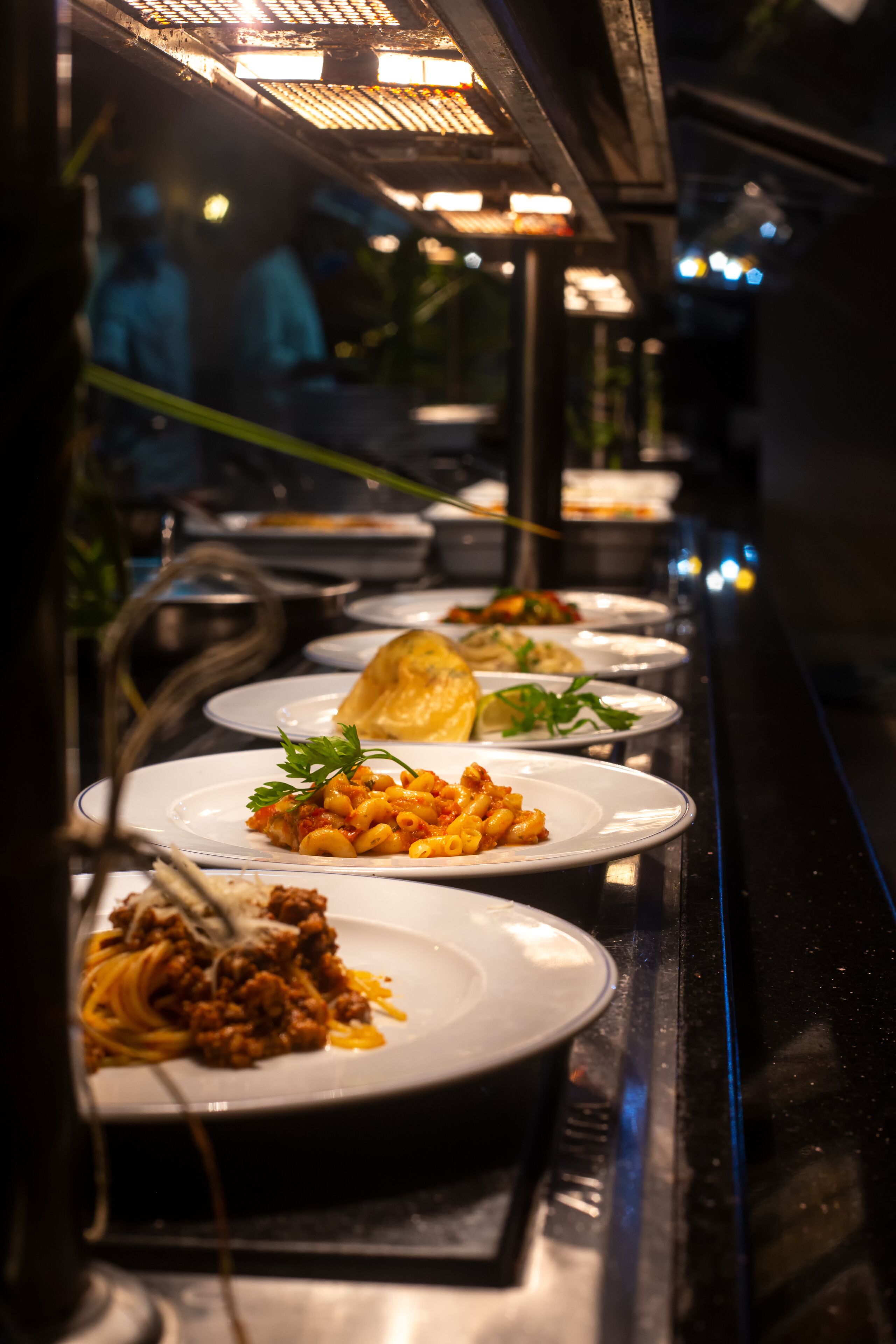 Un buffet proposant divers plats, notamment des pâtes et un plat de viande, le tout éclairé par un projecteur lumineux placé au-dessus.