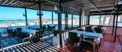 An outdoor restaurant with tables and chairs, overlooking a beach.