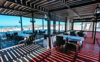 Un restaurante al aire libre con mesas y sillas, con vistas a la playa.