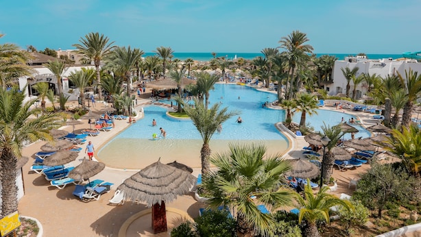 A resort pool area with multiple swimming pools, sun loungers, and palm trees. - Hotel Fiesta Beach Djerba (Djerba Midun)