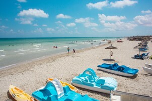 Una playa con varias embarcaciones acuáticas, incluyendo lanchas inflables y kayaks, y una fila de sillas y sombrillas de playa.