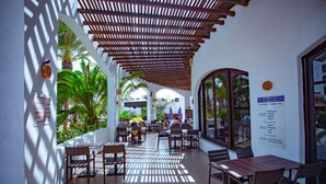 An outdoor café with wooden tables and chairs, surrounded by white walls and covered by a wooden pergola. - Hotel Fiesta Beach Djerba (Djerba Midun)