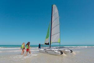Un velero en la playa con dos personas caminando a su lado.