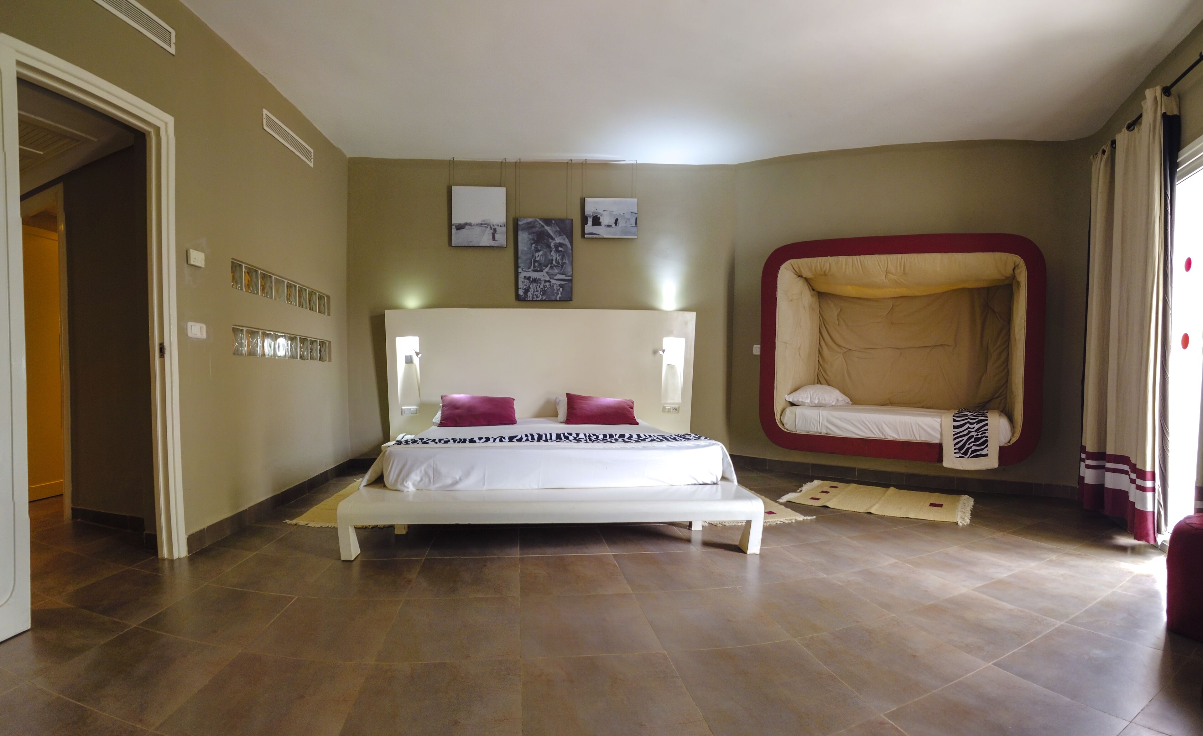Een slaapkamer met een groot bed, een slaapbank en een wandplank met decoratieve objecten.
