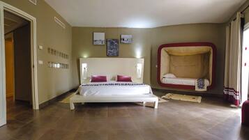 Een slaapkamer met een groot bed, een slaapbank en een wandplank met decoratieve objecten.