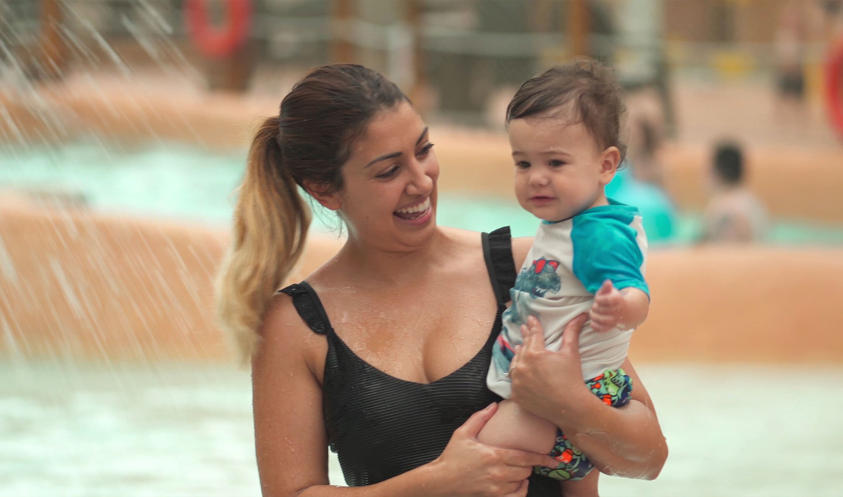 A woman holding a child near a water feature.