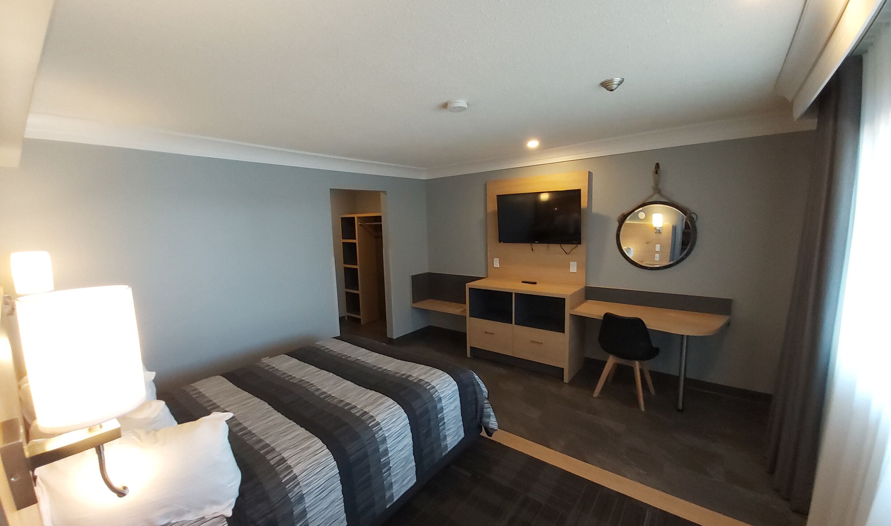 Une chambre d’hôtel équipée d’un lit, d’un bureau, d’une chaise, d’une télévision, d’un miroir et d’une armoire.