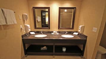 A hotel bathroom with two sinks, a hairdryer, and a mirror.