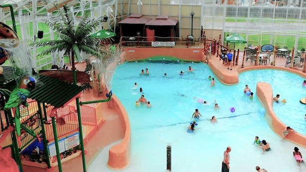 Una piscina interior con varias pistas de natación, una zona poco profunda y un área de juegos con toboganes y una decoración de palmera.