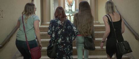 A group of women descending a grand staircase in a building with ornate architecture and a chandelier.