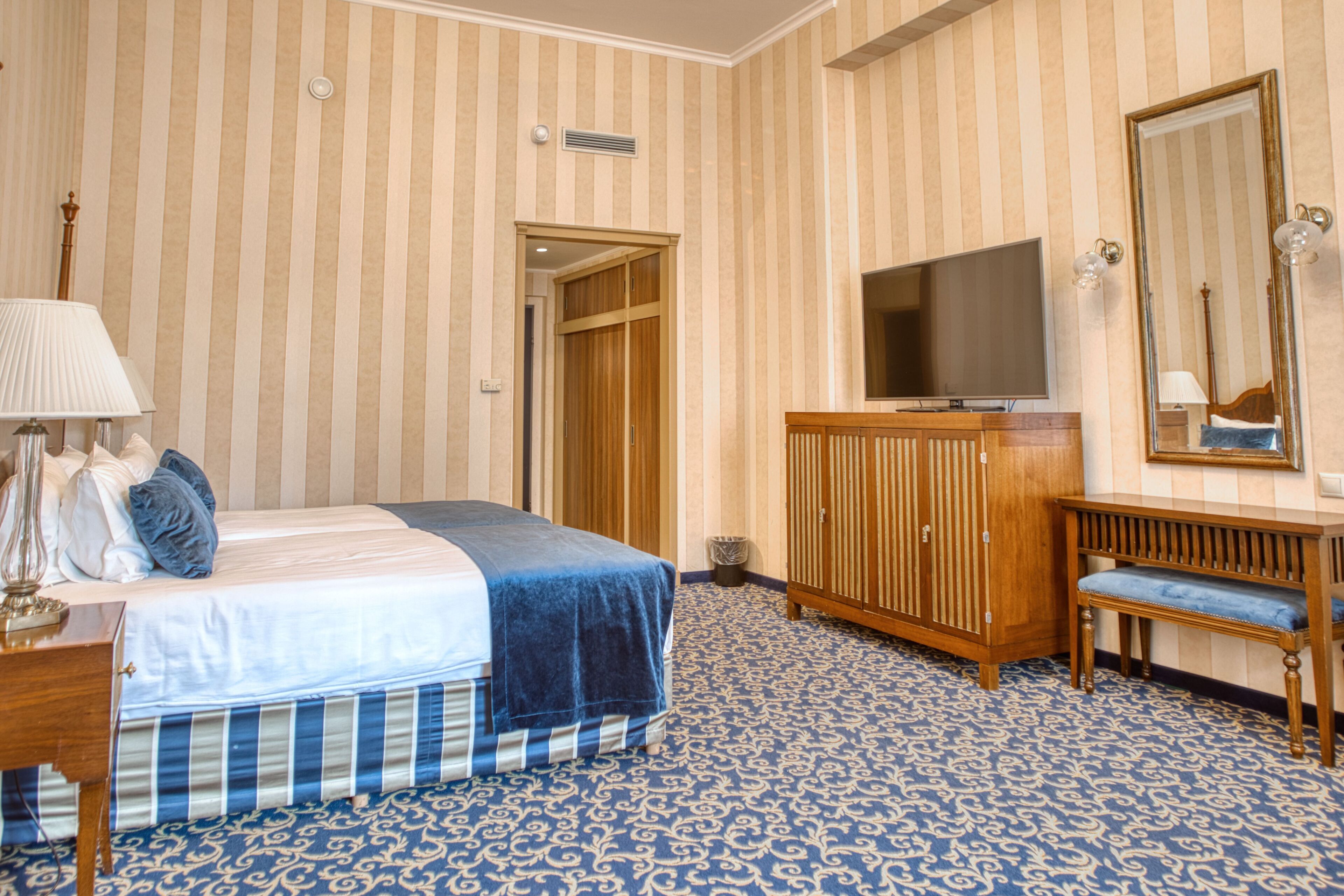 A hotel room with a bed, a television, a mirror, and a wooden cabinet.