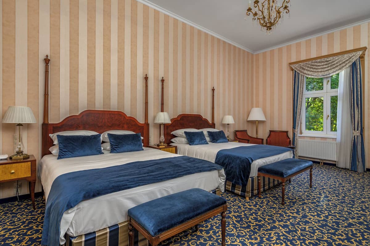 Ein Hotelzimmer mit zwei Betten, gestreifter Tapete, einer Chandelier und einem gemusterten Teppich.