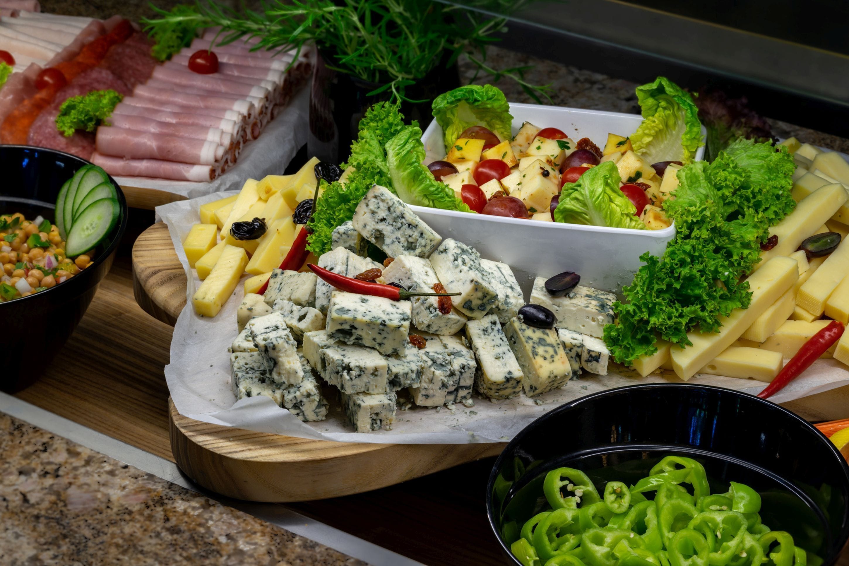 Diversos queijos, embutidos e uma salada sobre uma tábua de madeira.