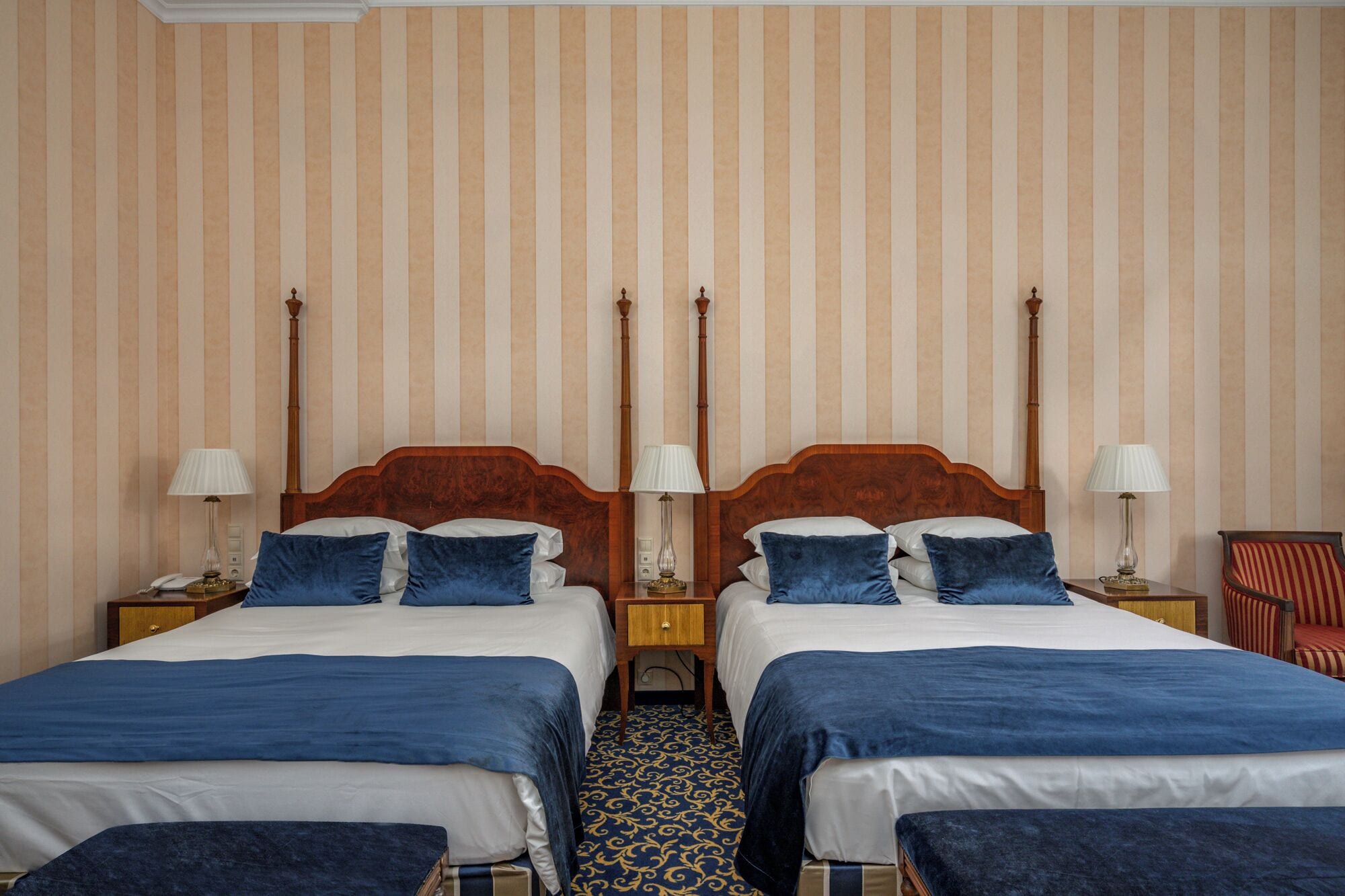 A hotel room with two beds, striped wallpaper, and a patterned floor.